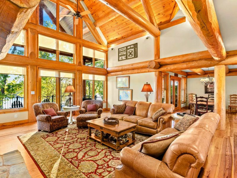Great Room - Floor-to-ceiling A-frame windows flood the room with natural light while leather seating and a red area rug anchor the space.
