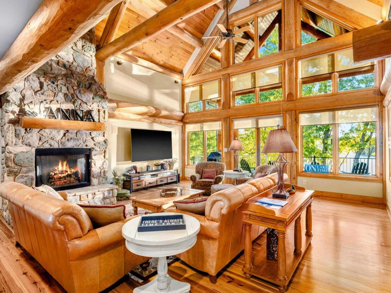 Cozy and elegant log cabin interior featuring a grand stone fireplace, high vaulted ceilings, and warm natural lighting