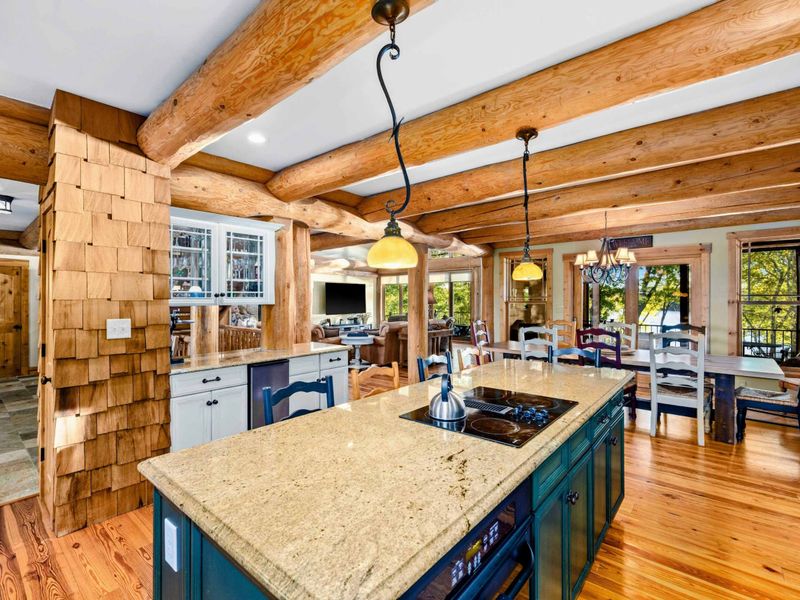 Kitchen - Island with cooktop and pendant lighting opens to the dining area, with cedar shake accents and log beams throughout.