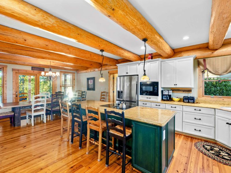 Kitchen - Bar stools at the island, white cabinetry, stainless steel appliances, and a view through to the dining area.