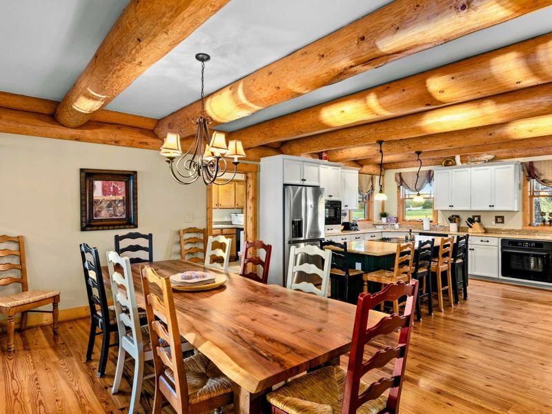 Dining Room - Long farmhouse table beneath log beam ceilings and a classic chandelier, open to the kitchen.