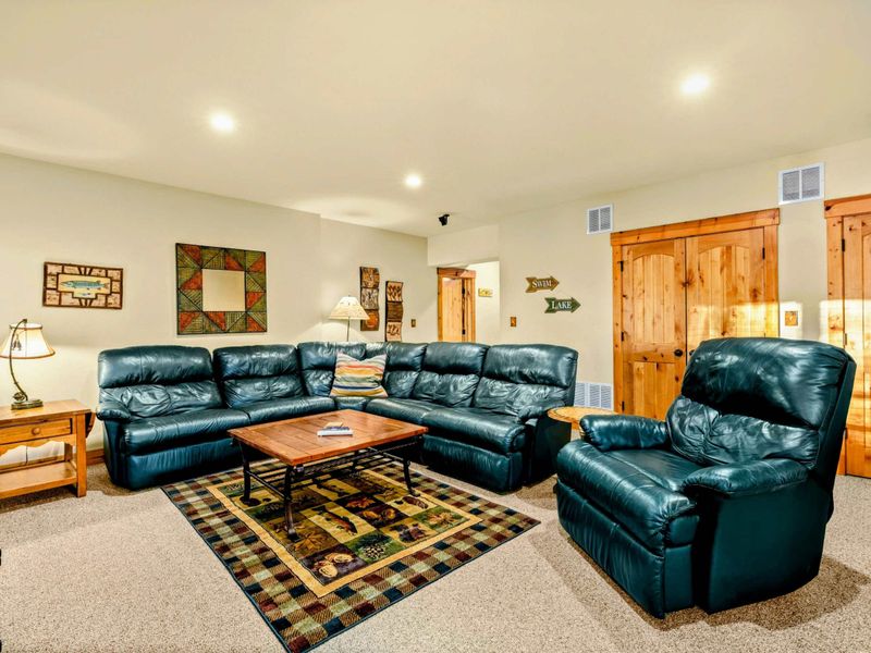 Lower Level Family Room - Green leather sectional and recliner with a plaid area rug and rustic knotty pine doors.