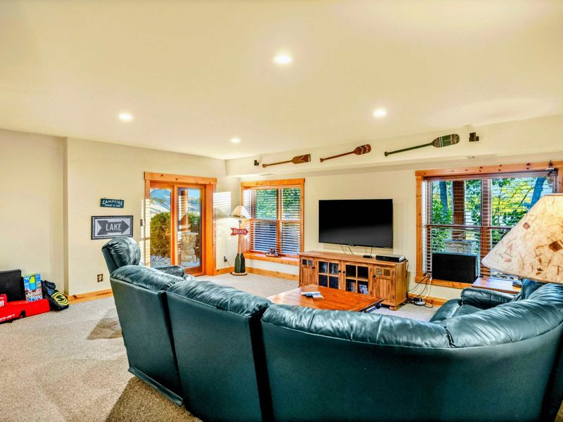 Lower Level Family Room - Dark green leather sectional faces a large TV with lake-themed decor and French doors opening to the patio.