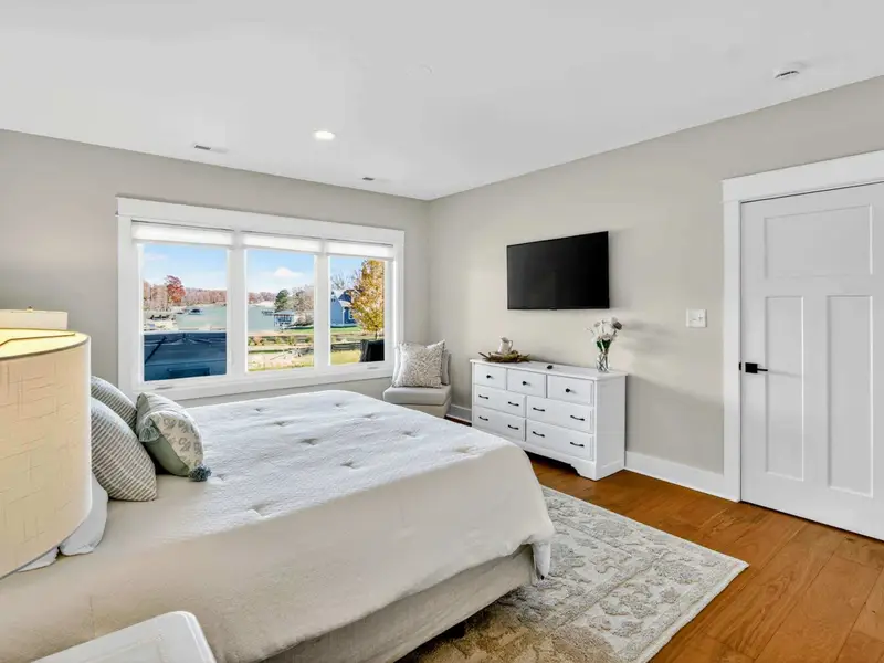 Lower Level King Suite View - The Smart TV, white dresser, accent chair, and lake views through the picture window in this lower-level retreat. This king suite feels very private and even has a view of the hot tub with the lake beyond!