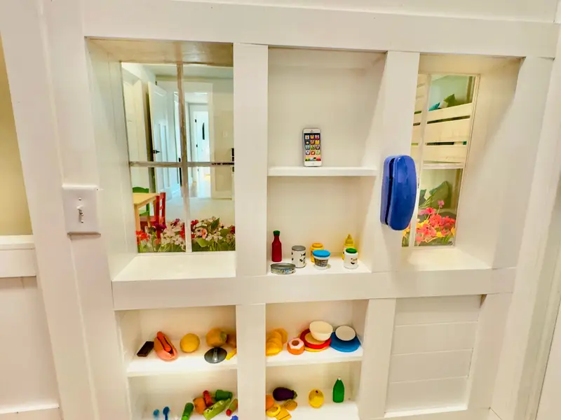 Market Window - The playhouse window with built-in display shelves full of play food, a toy phone, and a view into the bunk room.
