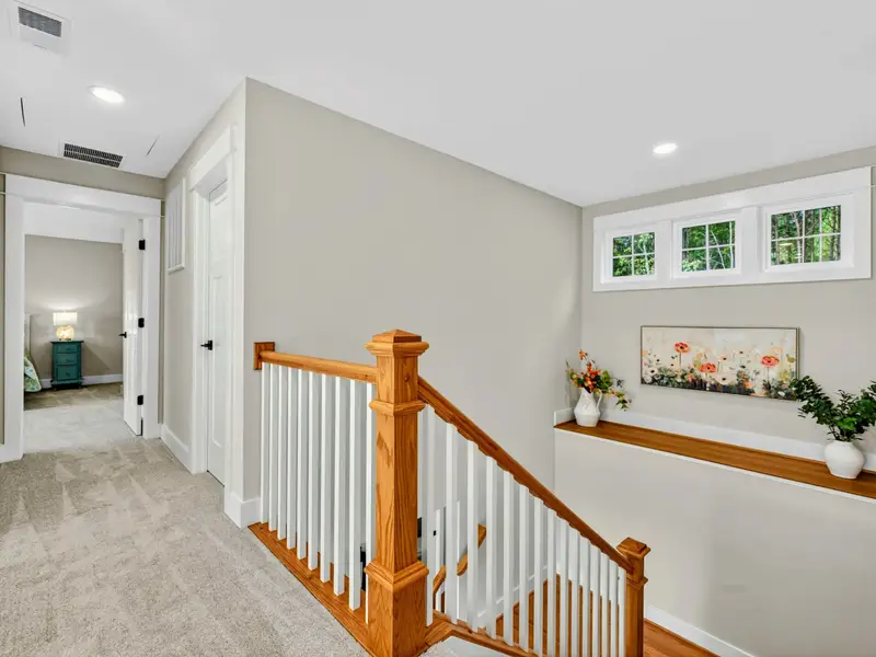 Upper Level Landing - The top of the staircase opens to a bright hallway with clerestory windows, floral artwork, and entries to both upper king suites.