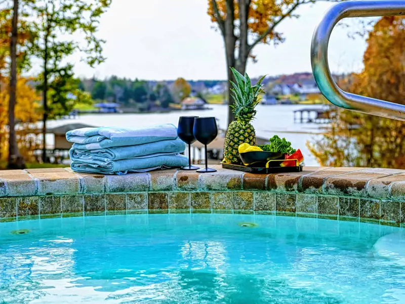 Resort-style heated pool with a built-in spa shelf and baja loungers in the water, framed by full lake views.