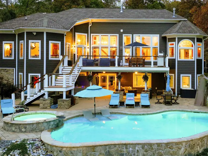 Resort-style heated pool with a built-in spa shelf and baja loungers in the water, framed by full lake views.