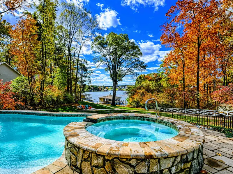 Resort-style heated pool with a built-in spa shelf and baja loungers in the water, framed by full lake views.