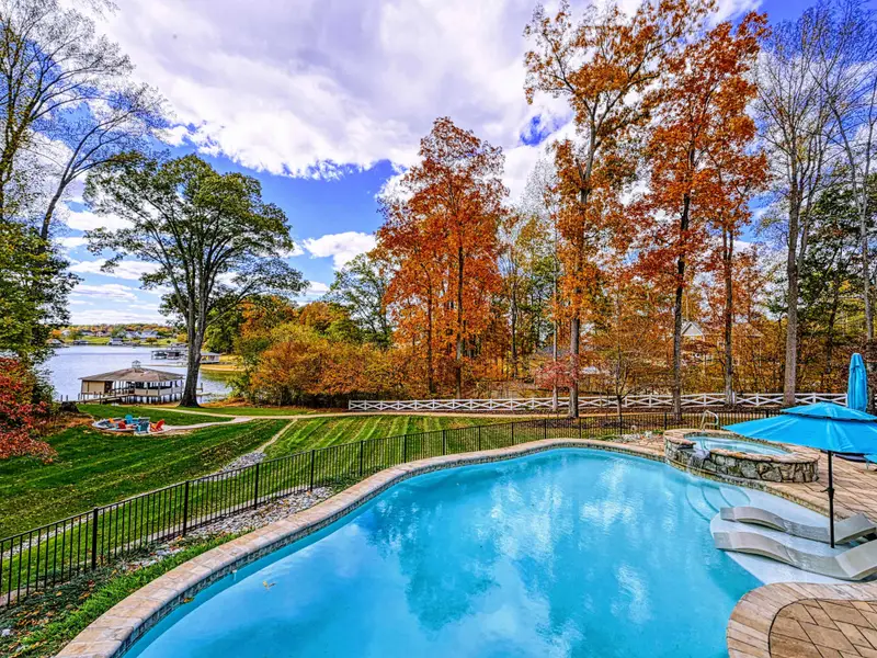 Resort-style heated pool with a built-in spa shelf and baja loungers in the water, framed by full lake views.