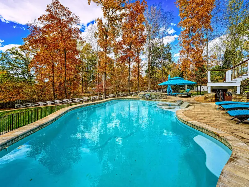 Resort-style heated pool with a built-in spa shelf and baja loungers in the water, framed by full lake views.