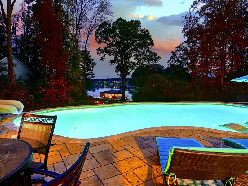 Resort-style heated pool with a built-in spa shelf and baja loungers in the water, framed by full lake views.
