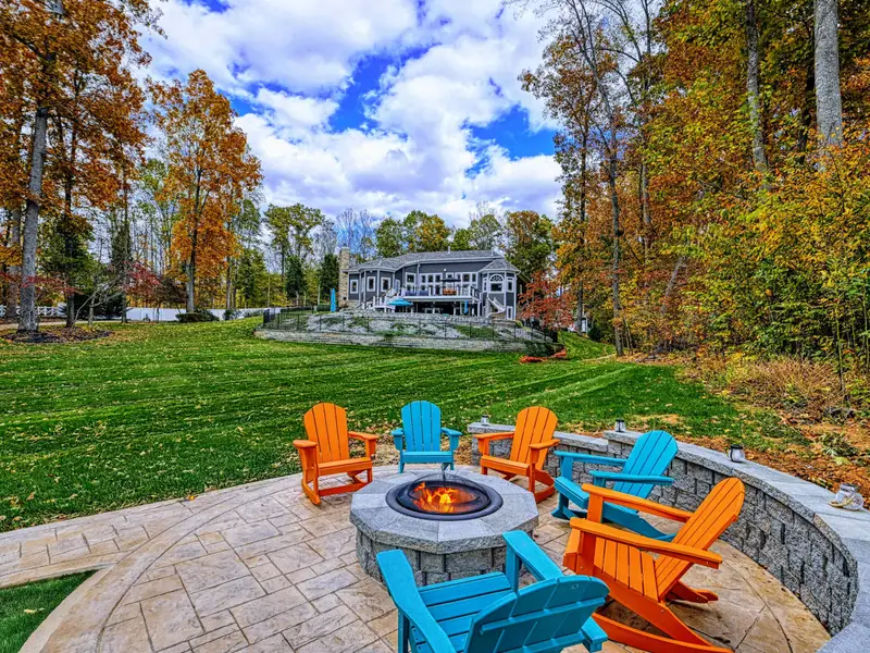 Lit fire-pit circle tucked into the hillside with Adirondacks in bright, joyful lagoons of color — sunset here feels like a ritual.