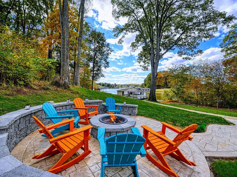 Lit fire-pit circle tucked into the hillside with Adirondacks in bright, joyful lagoons of color — sunset here feels like a ritual.