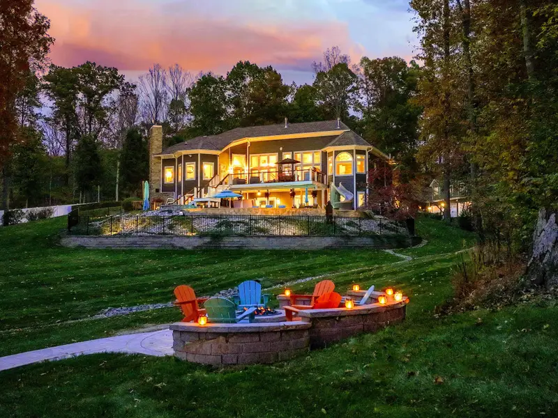 Lit fire-pit circle tucked into the hillside with Adirondacks in bright, joyful lagoons of color — sunset here feels like a ritual.