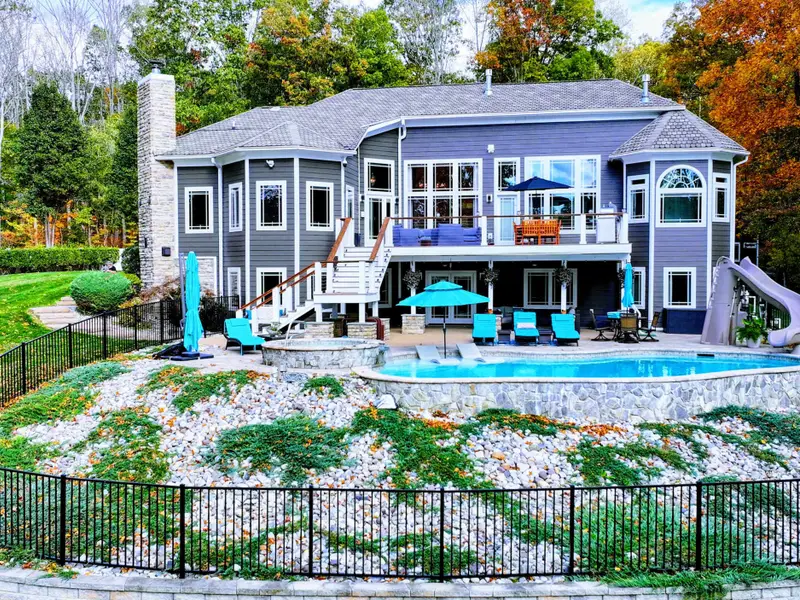 Resort-style heated pool with a built-in spa shelf and baja loungers in the water, framed by full lake views.
