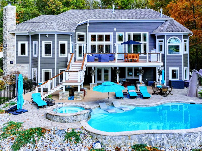 Resort-style heated pool with a built-in spa shelf and baja loungers in the water, framed by full lake views.