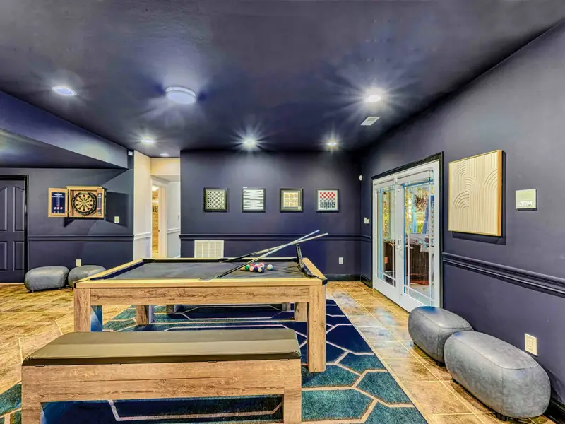 The Billiard & Games Lounge is a lower-level play hub with a convertible pool/ping-pong/dining table, darts, arcade and wall games, leather swings, and direct patio access—designed for laughter, competition, and all-ages fun.