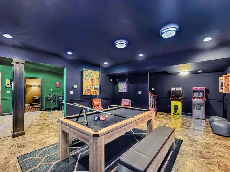 The Billiard & Games Lounge is a lower-level play hub with a convertible pool/ping-pong/dining table, darts, arcade and wall games, leather swings, and direct patio access—designed for laughter, competition, and all-ages fun.