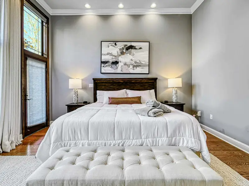The Primary Suite is a private retreat with a king bed dressed in hotel-quality linens, floor-to-ceiling windows with serene views, automatic shades, a 65” Smart TV, walk-in closet, and French doors to the deck—designed for deep rest and unhurried la