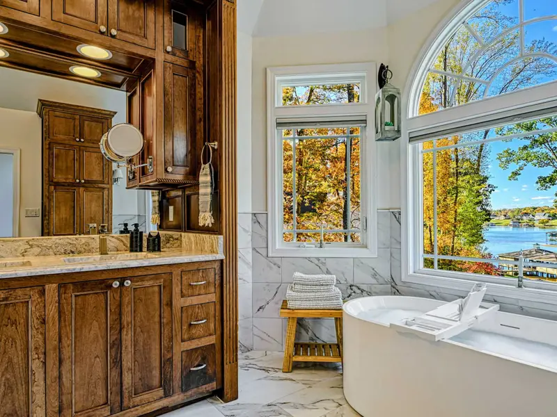 The Primary Ensuite is a spa-like retreat featuring a soaking tub with lake views, arched windows, and an oversized walk-in shower with dual heads and bench—designed for quiet mornings, slow evenings, and total relaxation.