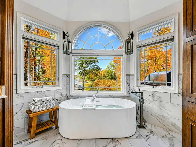 The Primary Ensuite is a spa-like retreat featuring a soaking tub with lake views, arched windows, and an oversized walk-in shower with dual heads and bench—designed for quiet mornings, slow evenings, and total relaxation.