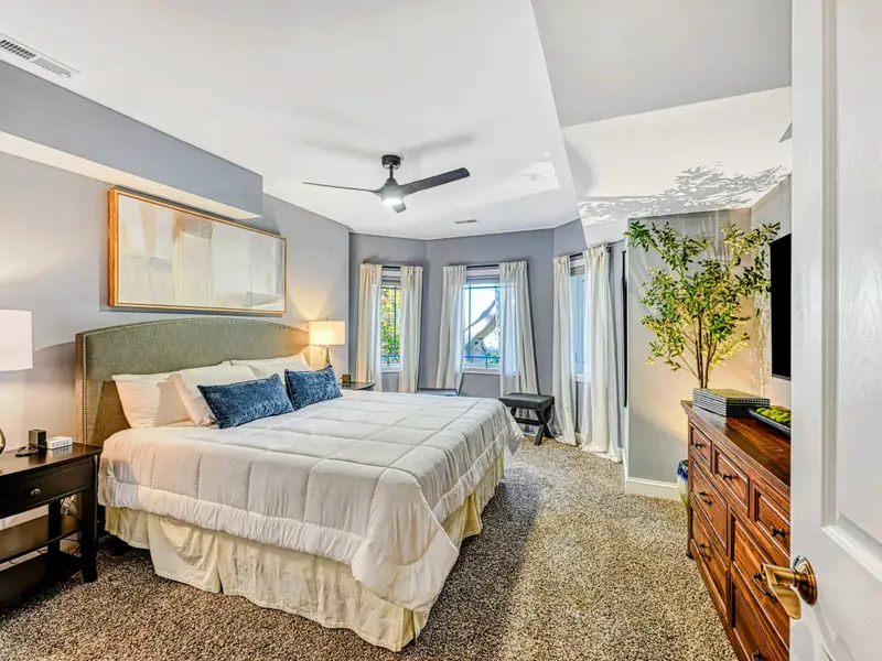 King Bedroom: Soft blue-gray retreat with plush king bed, luxury linens, smart TV, ceiling fan, roomy closet, cozy window seating, and access to a shared hall bathroom.