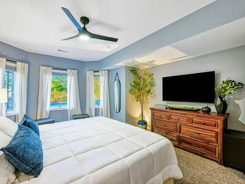 King Bedroom: Soft blue-gray retreat with plush king bed, luxury linens, smart TV, ceiling fan, roomy closet, cozy window seating, and access to a shared hall bathroom.