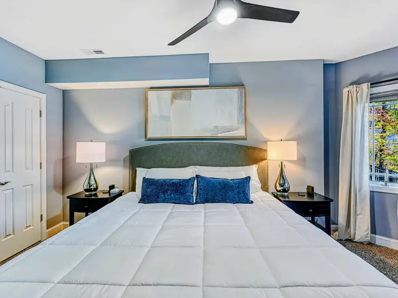 King Bedroom: Soft blue-gray retreat with plush king bed, luxury linens, smart TV, ceiling fan, roomy closet, cozy window seating, and access to a shared hall bathroom.