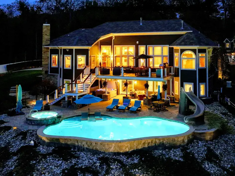 Resort-style heated pool with a built-in spa shelf and baja loungers in the water, framed by full lake views.
