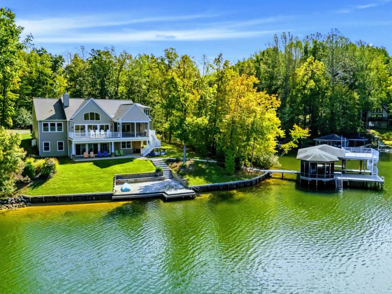 Waterfront View - The whole property from across the cove, home and tiered decks above a sweeping lawn that meets the private dock and boathouse.