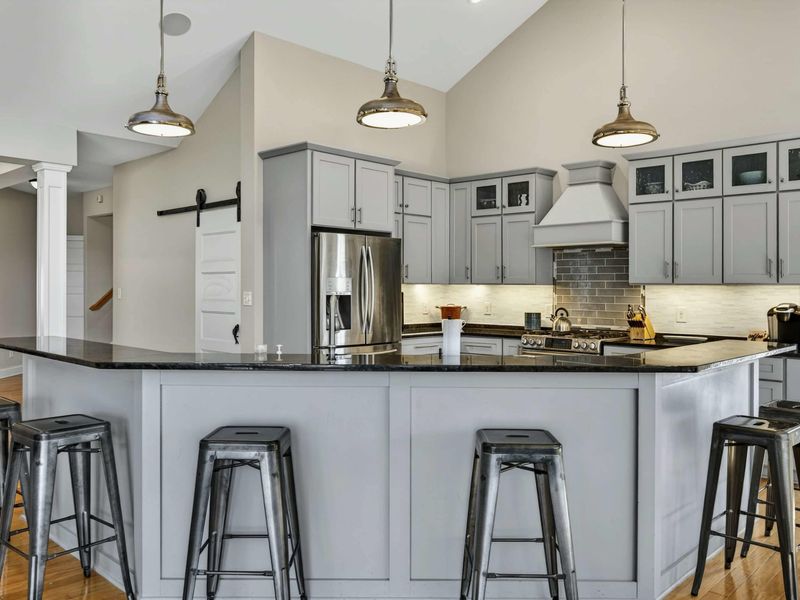 Kitchen - Gourmet kitchen with gray cabinetry, black granite island, industrial pendants, and bar seating for six.