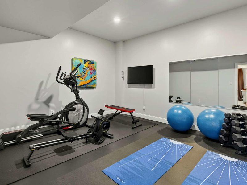 Fitness Room - Fully equipped gym with elliptical, weights, yoga mats, and a wall mirror.