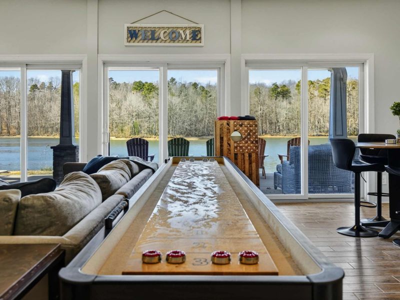 Lower Level - Shuffleboard table and lounge seating with sweeping lake views through floor-to-ceiling windows.