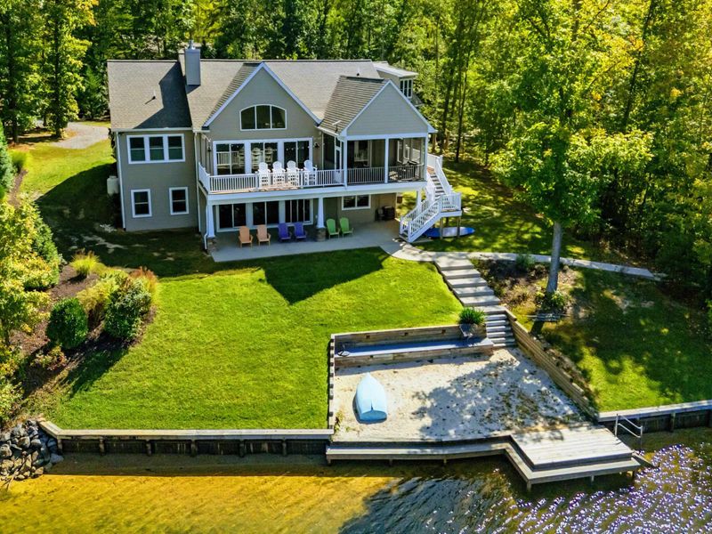 Aerial View - Full rear property view showing the deck, yard, fire pit, sandy beach, and dock.