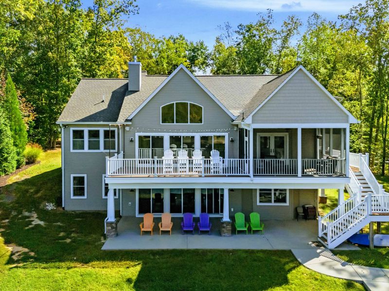 Rear Exterior - The full rear of the home from the yard, multi-level decks and screened porch above colorful Adirondack chairs on the patio.
