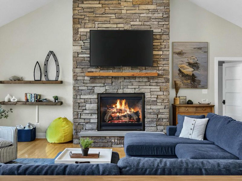 Great Room - Floor-to-ceiling stone gas fireplace with wood mantel, mounted TV, and floating shelves.