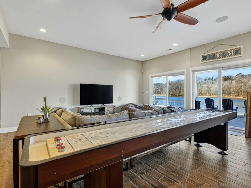 Lower Level - Shuffleboard table and TV lounge with panoramic lake views through sliding glass doors.