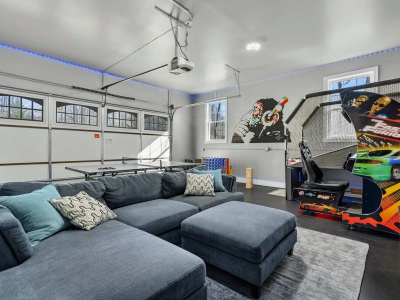 Game Room - Sectional sofa faces the large TV, flanked by arcade machines with blue LED accent lighting.