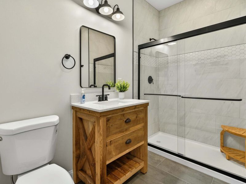 Lower Bathroom - Rustic wood vanity with glass walk-in shower featuring marble-look tile.