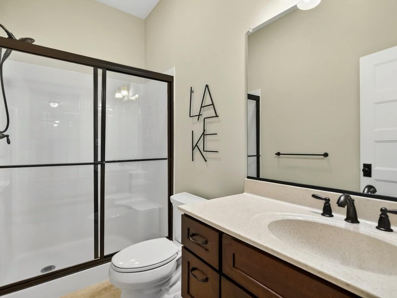 Bathroom - Walk-in shower with glass door, single vanity, and playful LAKE wall art.