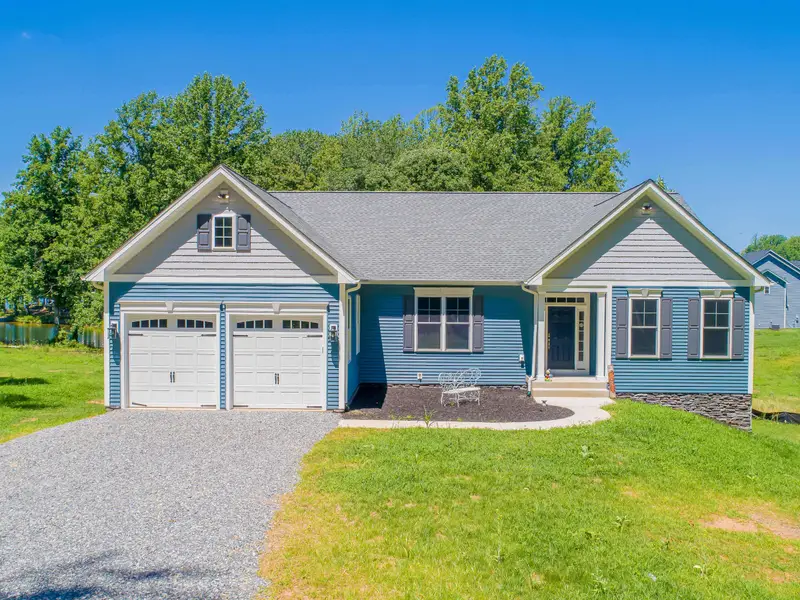 Exterior - Blue craftsman-style ranch with a two-car garage, gabled entry, and a welcoming gravel driveway surrounded by green lawn.