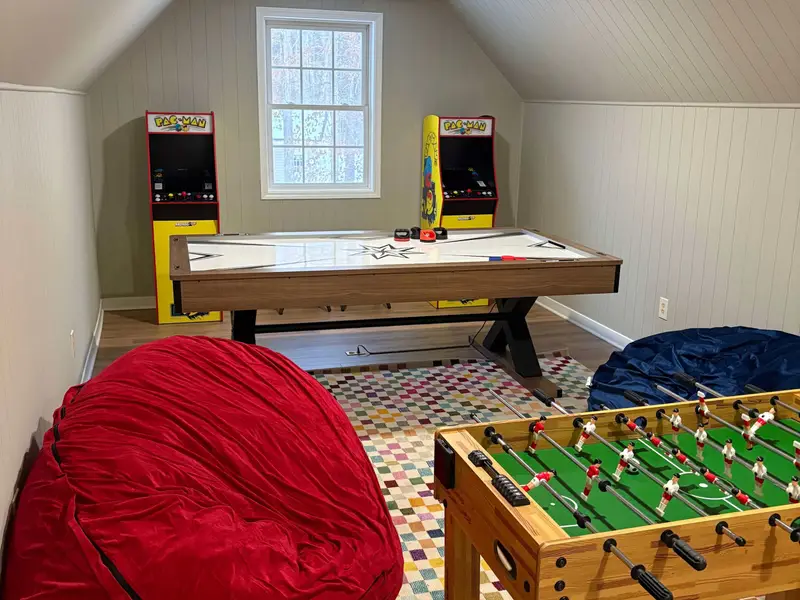 Game Room - Attic game room with air hockey table, foosball, two arcade cabinets, bean bag seats, and a colorful rug under natural light.