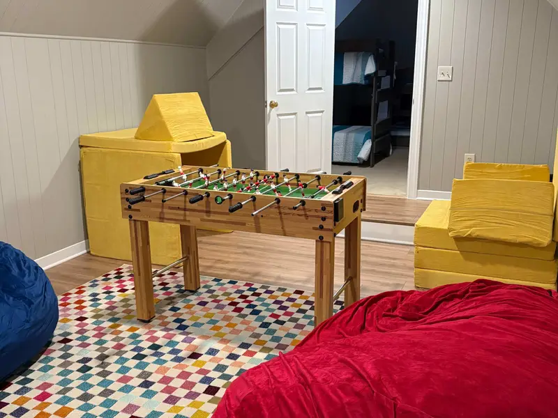 Game Room - Alternate angle showing the foosball table, yellow foam chairs, bean bags, and a doorway to the bunk room.