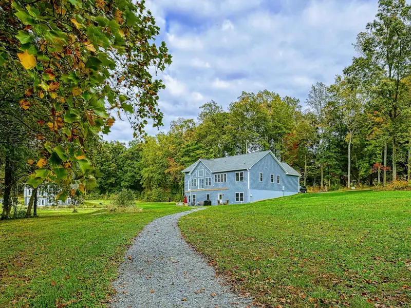 Exterior - Winding pathway through the manicured lawn leads to the blue-sided home nestled among mature hardwoods.