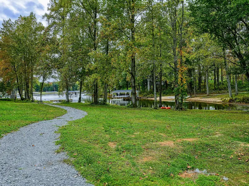 Grounds - Gravel pathway meanders through the green lawn toward the lake, with the dock and waterfront seating visible ahead.