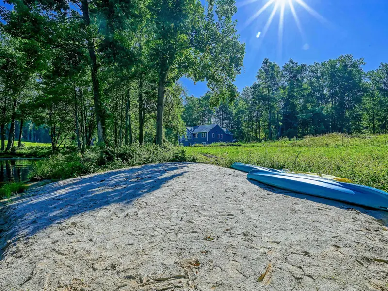 Waterfront - Sandy beach area with a kayak and paddleboard staged for easy lake access, looking back toward the home through the trees.