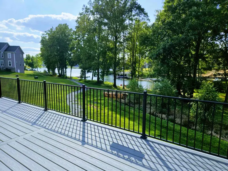 Upper Deck - Composite decking with black metal railings offers a relaxing perch overlooking the lake through mature trees.