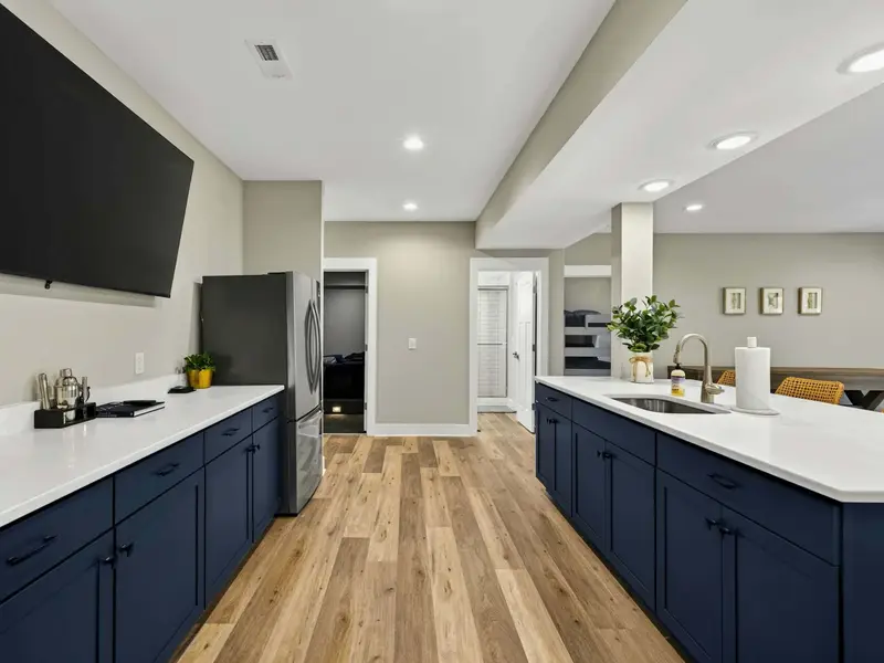Wet Bar Kitchen - Navy cabinetry, quartz counters, a large TV, and a full-size fridge anchor the lower-level entertaining space.