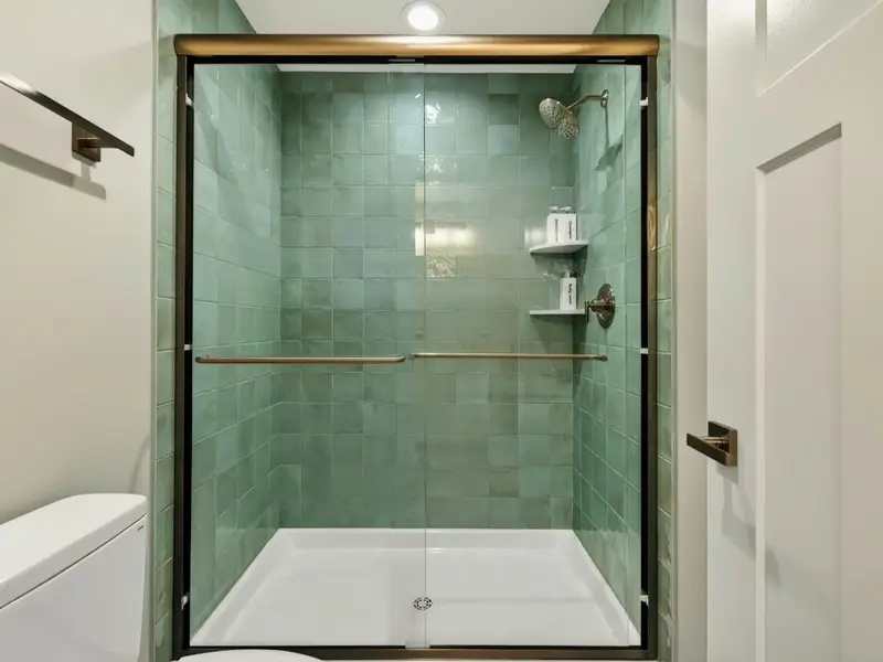 Walk-In Shower - A glass-enclosed shower with green tile and modern fixtures in the shared bath.